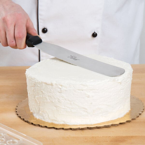 A person using an Ateco straight baking spatula with a black plastic handle to cut a cake.