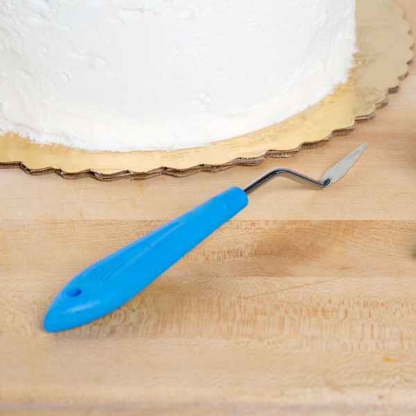 A cake with white icing next to an Ateco offset spatula on a wood surface.