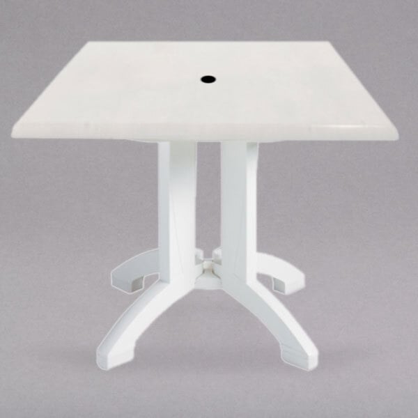 A white Grosfillex outdoor table with a square top and umbrella hole.