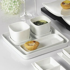 A white square porcelain CAC tasting tray on a table with wine glasses and liquid in a cup.