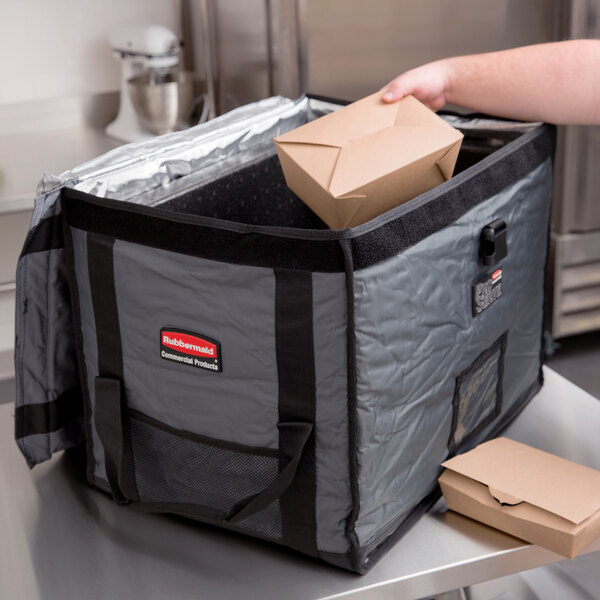 A person putting a Rubbermaid ProServe food pan carrier in a bag.