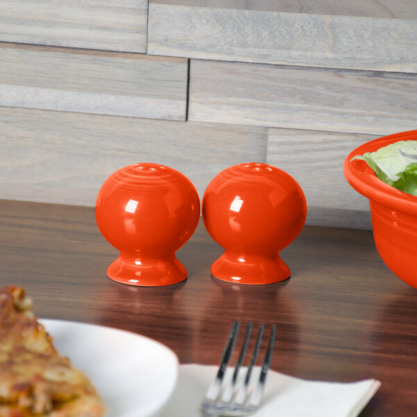 A Fiesta poppy pepper shaker on a table with a bowl of salad.