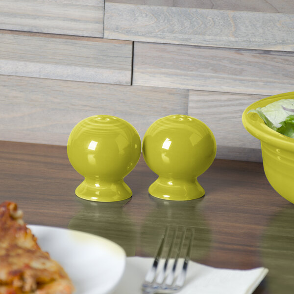 A yellow Fiesta pepper shaker on a table with a plate of pizza.