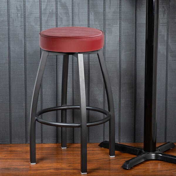 A Lancaster Table & Seating black bar stool with a red cushion.