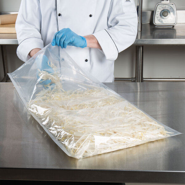 A chef holding a VacPak-It 18" x 28" vacuum packaging pouch of shredded cheese.