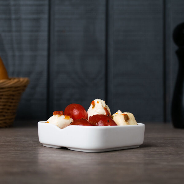 A white Arcoroc square porcelain bowl filled with food on a table.
