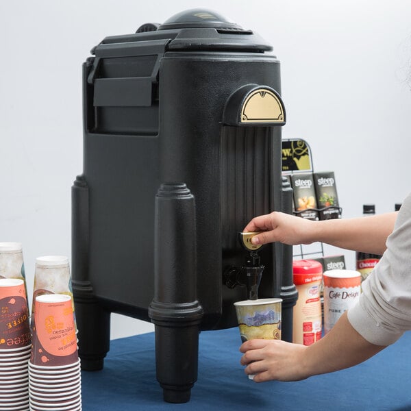 A woman using a Cambro black insulated beverage dispenser to pour coffee.
