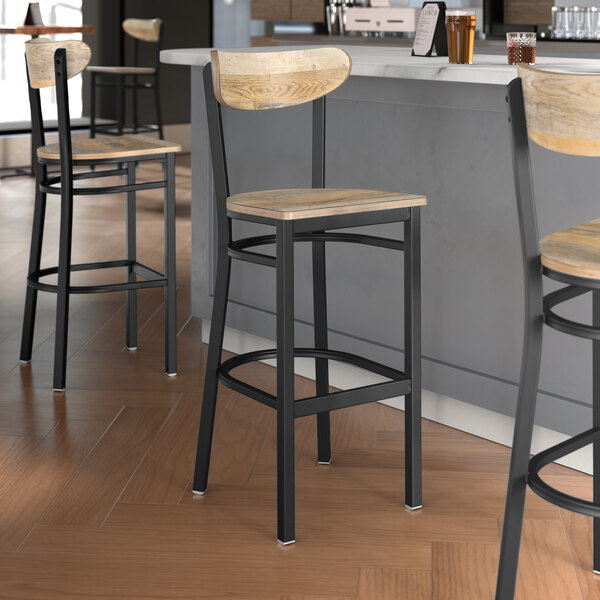 Three Lancaster Table & Seating Boomerang black bar stools with driftwood seats at a wooden table in a bar.