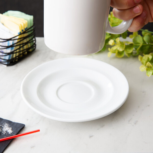 A hand holding a white Arcoroc porcelain saucer under a white mug.