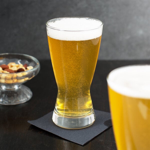 Two Libbey pilsner glasses of beer on a table with a bowl of nuts.
