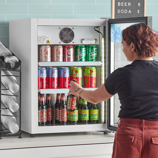 A woman opening an Avantco countertop display refrigerator with a beverage inside.