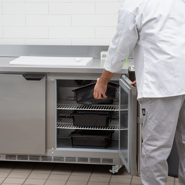 A man in a white shirt and white pants opens a Beverage-Air worktop freezer door in a school kitchen.