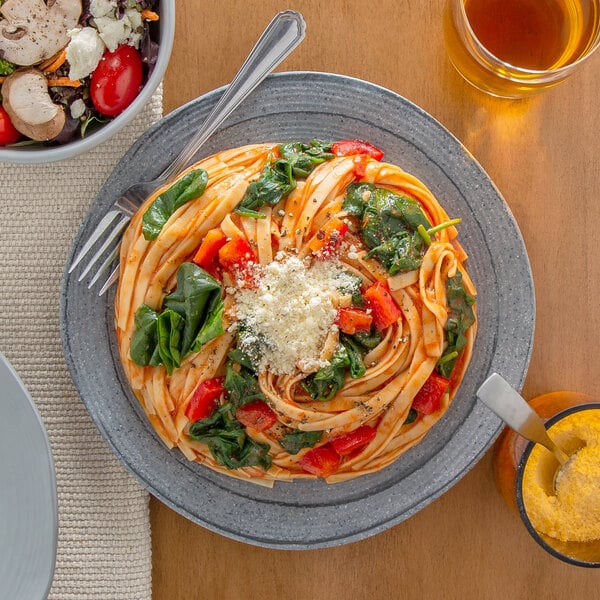 A plate of pasta with vegetables and cheese and a bowl of salad with tomatoes and mushrooms.