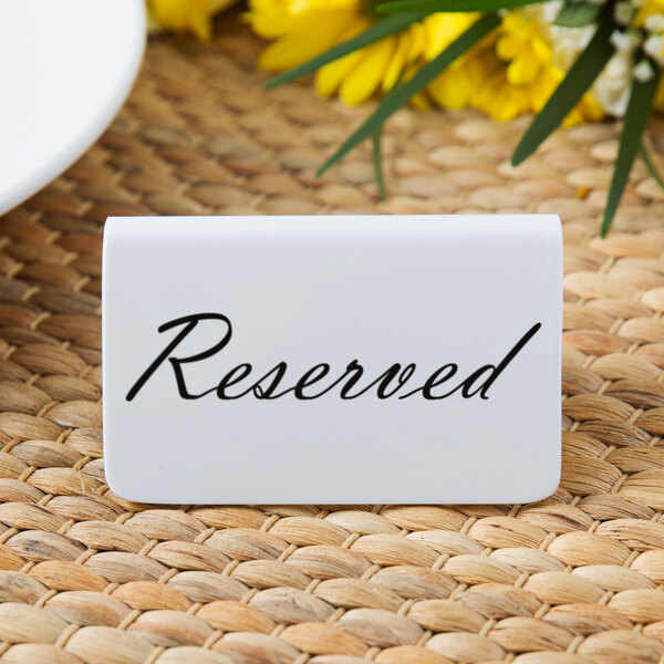 A white Tablecraft melamine table tent with black text that says "reserved" on it next to a plate and flowers.