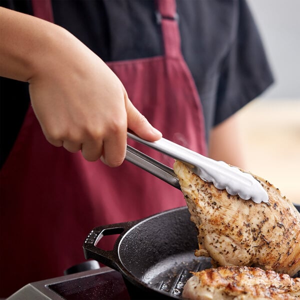 A person using Edlund heavy-duty scallop tongs to cook meat in a pan.