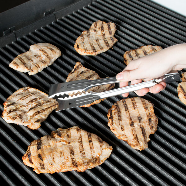 A person using Edlund heavy-duty tongs to grill meat.
