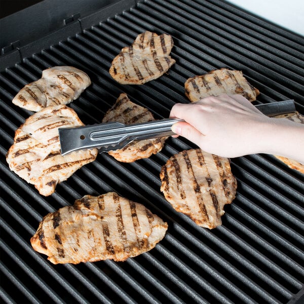A person using Edlund heavy-duty tongs to cook chicken on a grill.