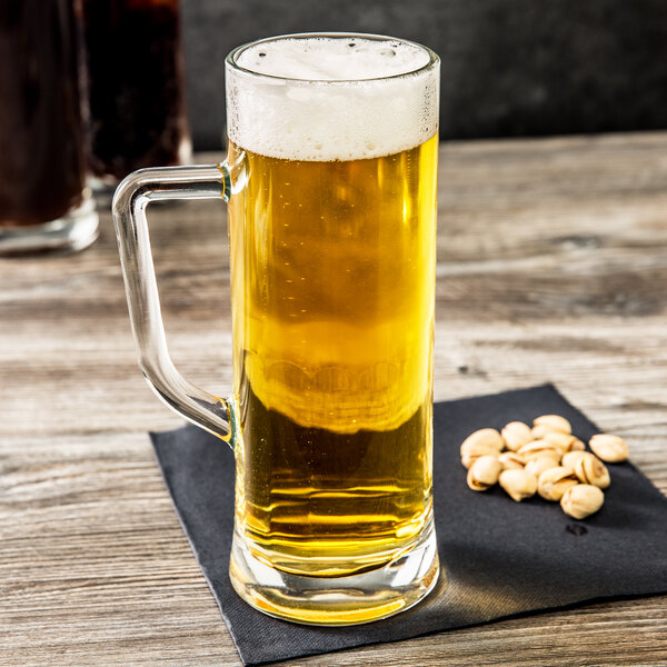 An Arcoroc glass mug of beer on a napkin with pistachios on it.
