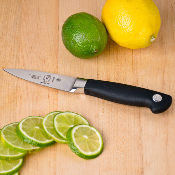 A Mercer Culinary Genesis forged paring knife with a black handle next to sliced limes on a cutting board.