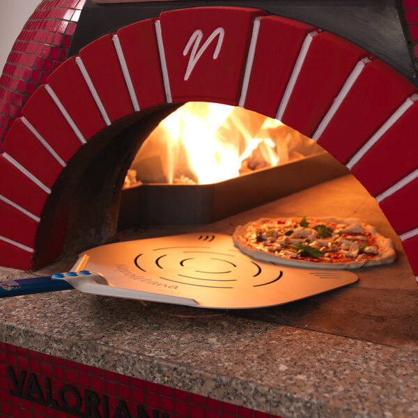 A pizza on a GI Metal square perforated pizza peel with a long handle being cooked in a pizza oven.