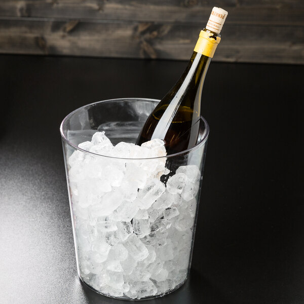 A bottle of wine in a clear polycarbonate wine bucket on a table.