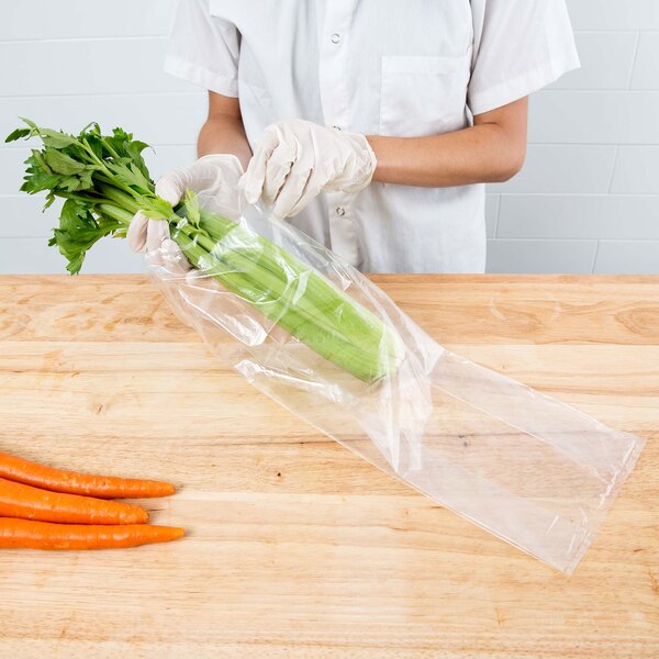 A person in gloves holding a bag of carrots and celery