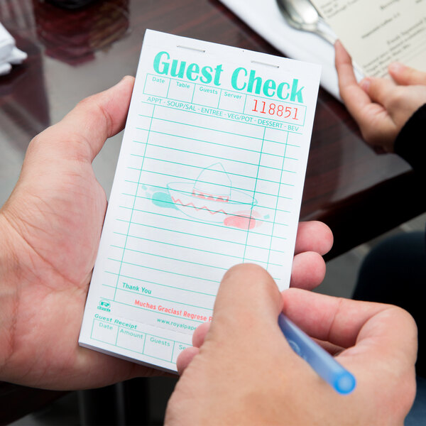 A hand holding a Royal Paper Mexican Themed guest check with a pen.
