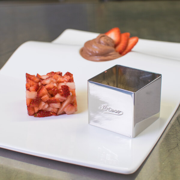 A white plate with a square piece of food next to a square stainless steel mold.