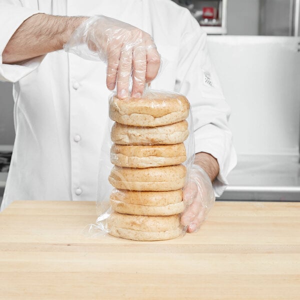 A man in a white coat putting a stack of bagels in a plastic bag.