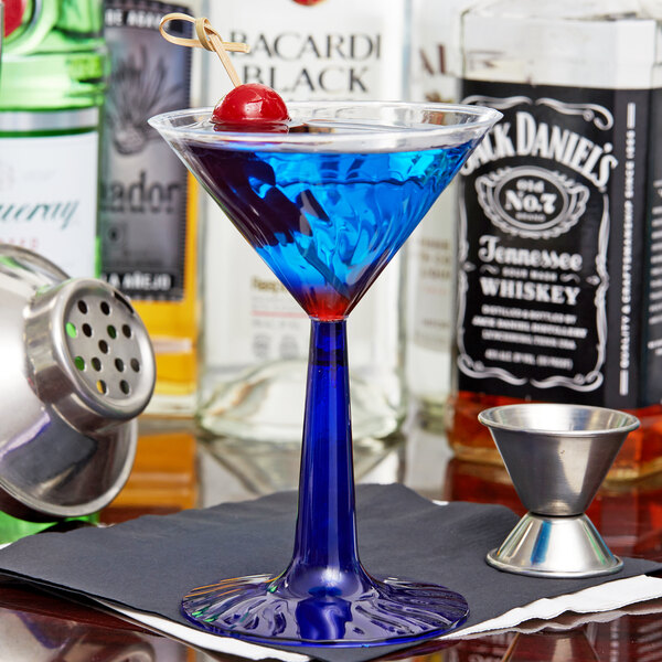 A close-up of a Fineline Flairware plastic martini glass with a cobalt blue base filled with a blue drink and a cherry.