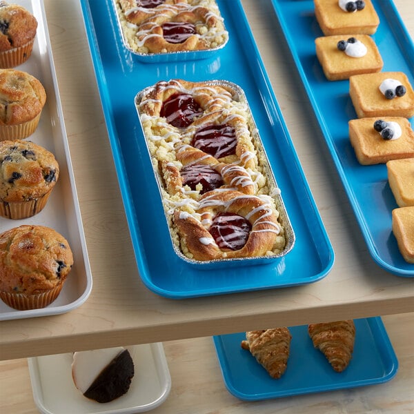 A blue Cambro market tray with a variety of pastries and muffins on a table.