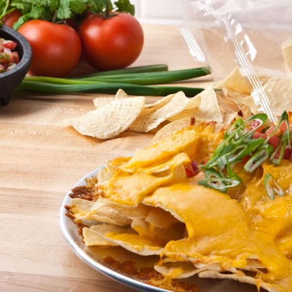 A plate of nachos with cheese and tomatoes served with Mission White Triangle Corn Tortilla Chips.