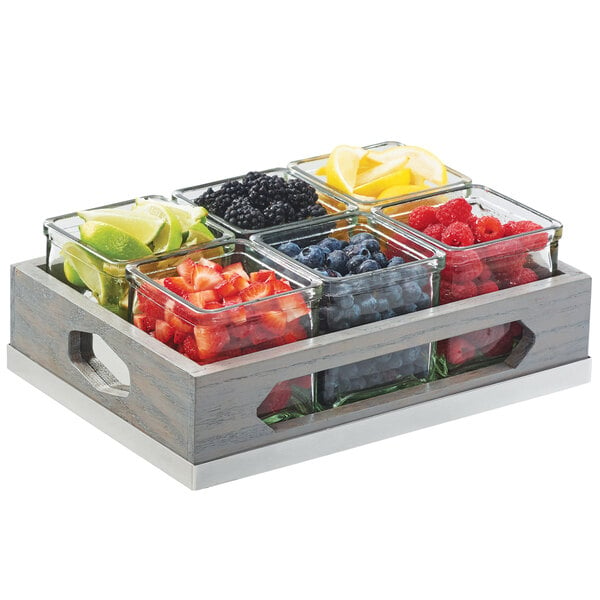 A Cal-Mil wooden organizer with glass jars of sliced fruit on a table.