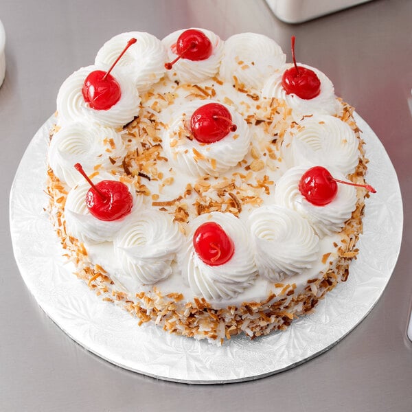A white round cake on a white Enjay cake drum with whipped cream and cherries on top.