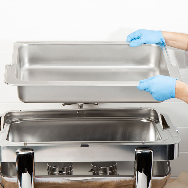 A person in blue gloves holding an Acopa metal water pan on a counter.