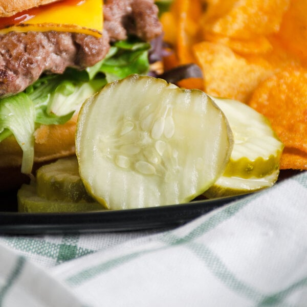 A plate of food with a burger and potato chips, a slice of Patriot Pickle next to it.
