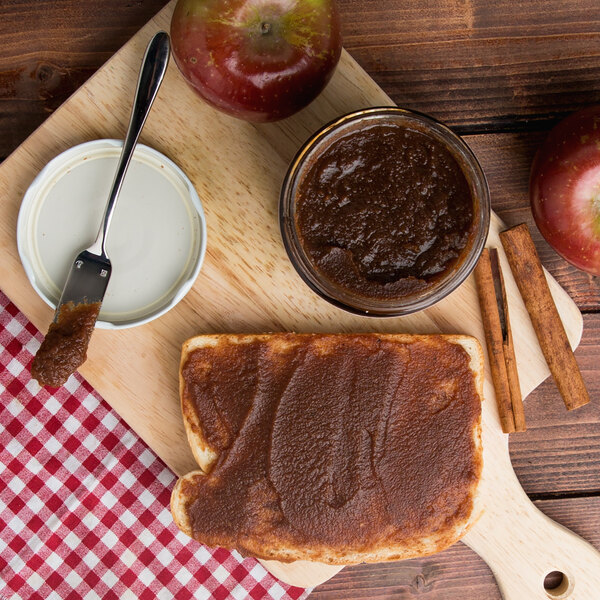 A piece of bread with Kime's apple butter next to a spoon and apples.