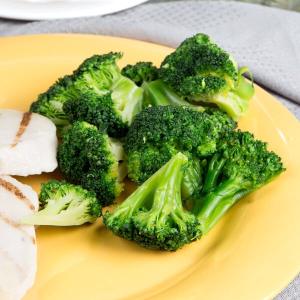 A yellow plate of broccoli and chicken with a side of broccoli.