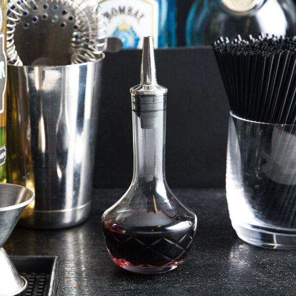 An American Metalcraft glass bitters bottle filled with a dark liquid on a bar counter.