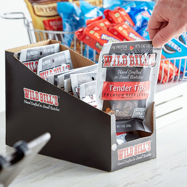 A hand holding a box of Wild Bill's Hickory Smoked Tender Tips beef jerky packets.