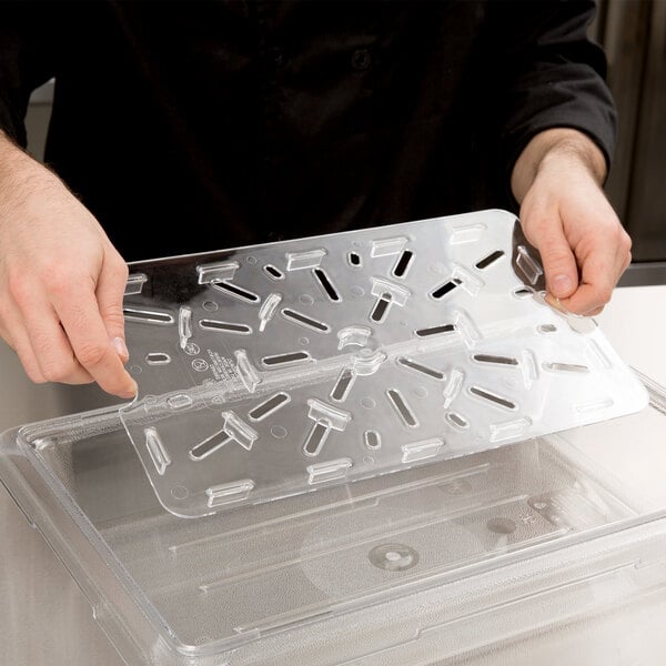 A person using a Cambro clear plastic food box drain tray on a counter.