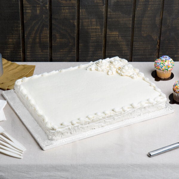 A white Enjay cake board under a white cake with white frosting on a table.
