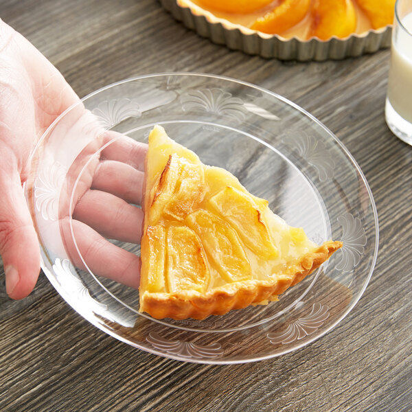 A hand holding a piece of pie on a clear plastic WNA Comet designerware plate.