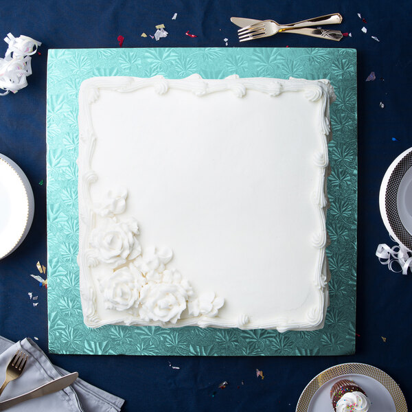 A white cake with white frosting on a blue Enjay square cake drum.