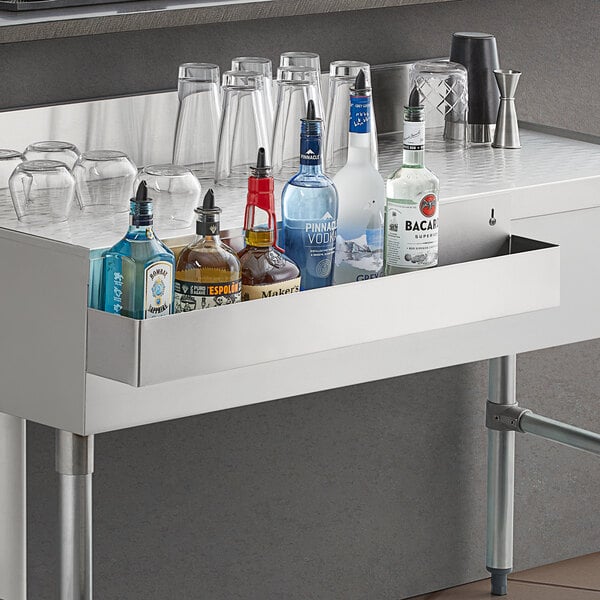 A Regency stainless steel speed rail on a counter with bottles and glasses in it.