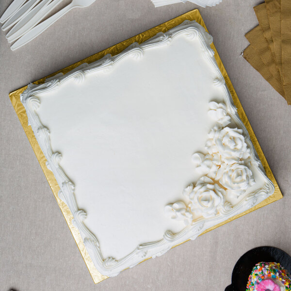 A white cake on a gold square cake board.