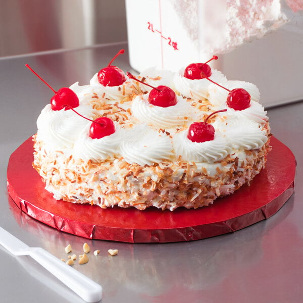 A cake with whipped cream and cherries on a red Enjay cake board.