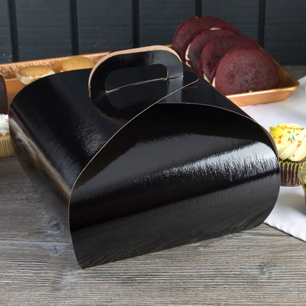 A black Enjay quad cupcake tulip box with a handle next to cupcakes.
