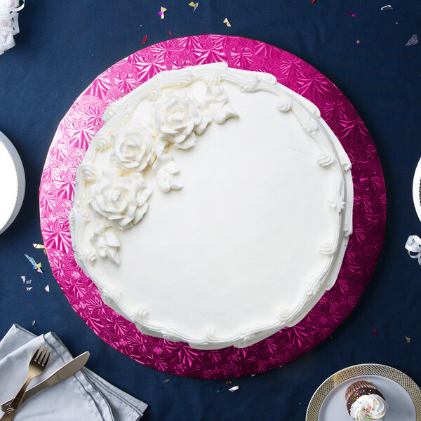 A white cake with white frosting and flowers on a pink Enjay cake drum on a white table.