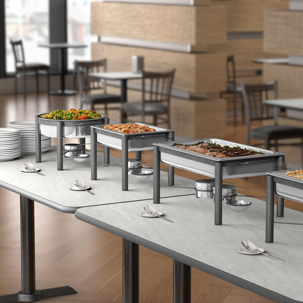 A buffet setup with several stainless steel chafing dishes on black metal stands, each containing different types of food, arranged on a white table in a restaurant setting.